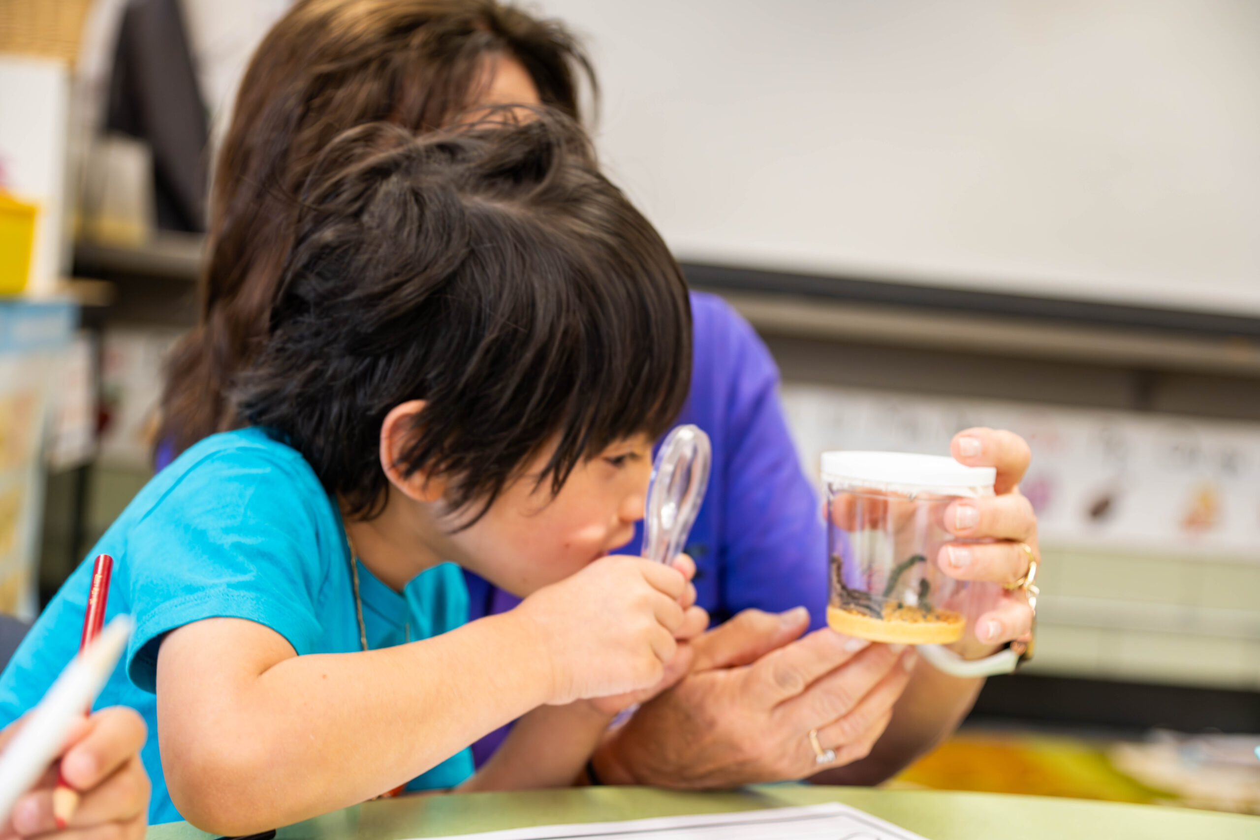 Preschool student looking through magnifying glass in class