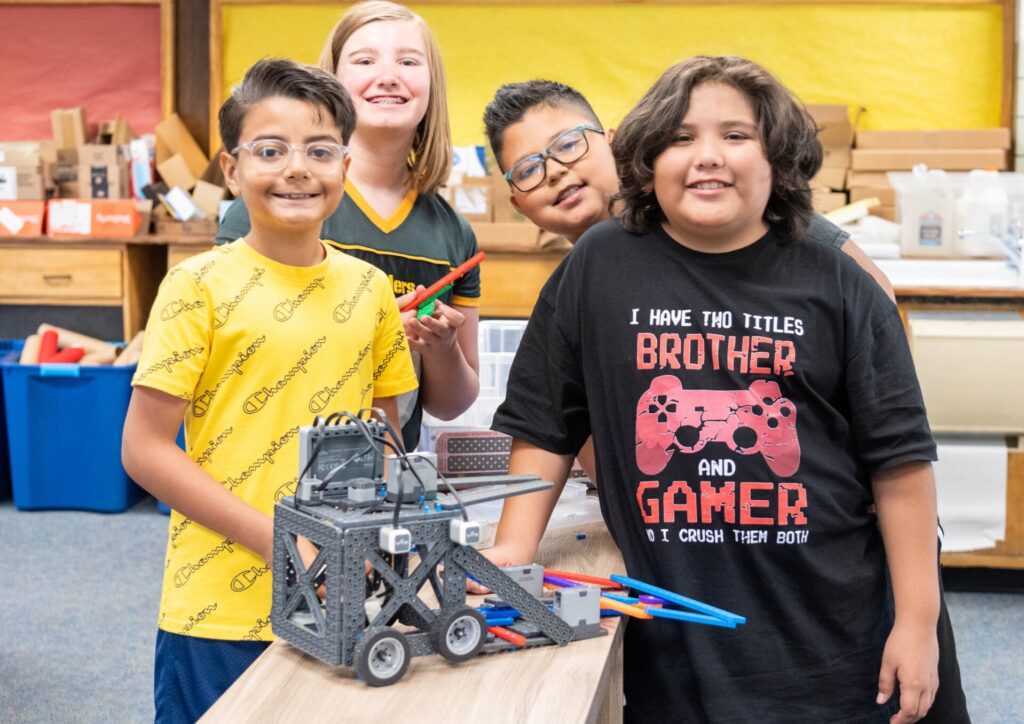 Four robotics students show off big smiles with their robot design. 