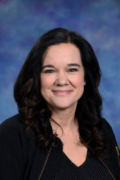 A woman with long, dark hair and a friendly smile poses in front of a blue and purple background.