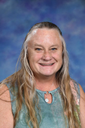 Smiling woman with long, wavy hair wearing a green top, set against a blue and purple background.