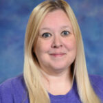 A woman with long blonde hair, wearing a purple shirt, smiles in front of a blue and purple backdrop.