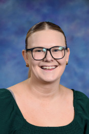 Smiling woman with glasses and a green top, against a blue and purple gradient background.