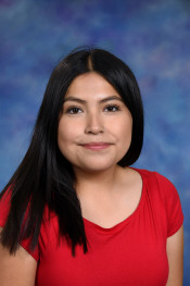 Una joven con el pelo largo y negro sonríe, vestida con una camiseta roja, sobre un fondo azul claro.