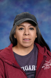 A woman with long dark hair wearing a black cap and a red hoodie, smiling against a blue background.