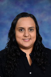 A woman with long, curly dark hair smiles, wearing a black shirt, set against a blue and purple background.