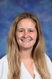 A smiling woman with long hair, wearing a white shirt, against a blue and purple background.