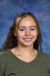 A young woman with curly hair smiles, wearing a green top, against a blue and purple gradient background.