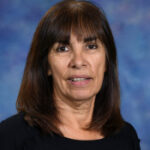 A woman with long dark hair and bangs, wearing a black top, smiles against a blue and purple gradient background.