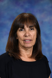 A woman with long dark hair and bangs, wearing a black top, smiles against a blue and purple gradient background.