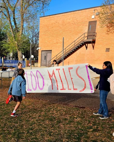 Niños sosteniendo una gran pancarta en la que se lee «¡100 MILES!» en un parque situado cerca de un colegio.