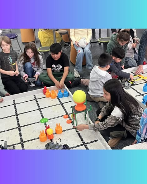 Children are engaged in a robotics activity, working with colorful pieces on a grid mat in a classroom setting.
