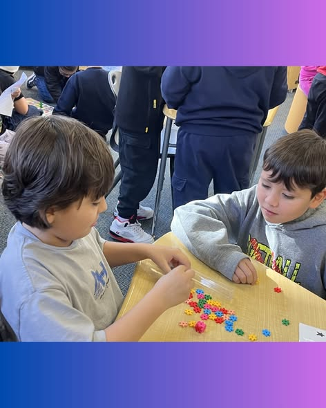 Dos niños están sentados a una mesa, concentrados en clasificar cuentas de colores con forma de estrella. Otros alumnos están ocupados en segundo plano.