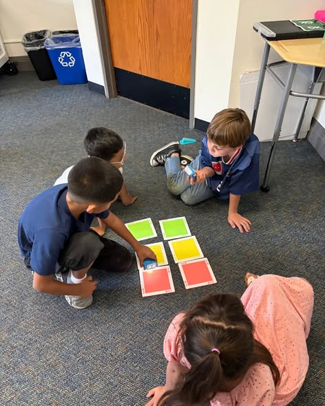 Four children interact with a small blue robot on colored square cards on the floor.